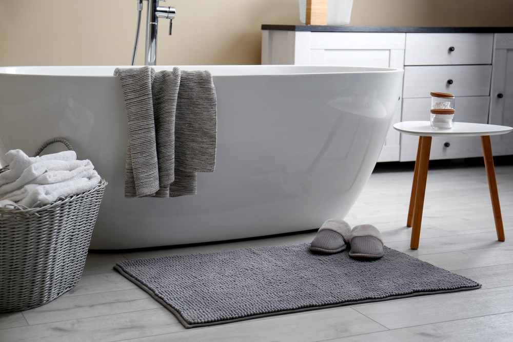 A gray bath mat in front of a large bath