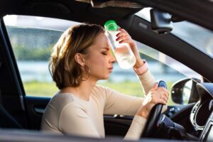 A stressed out woman in a car holding a cold bottle of water to her head. She has been doing too much for her aging parents and can't cope.