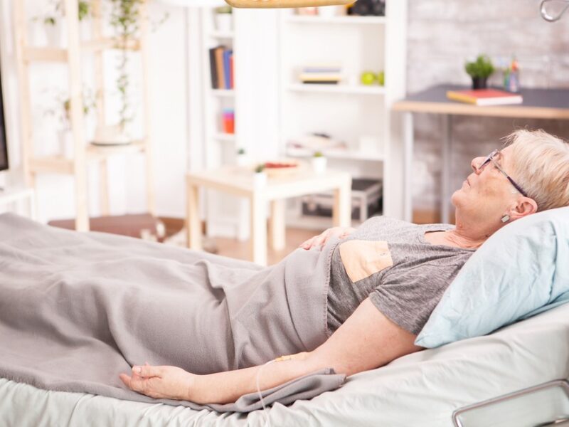 An older woman at home in a hospital bed, looking at the question of what is virtual hospice