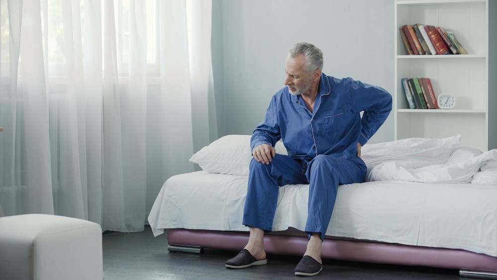 A senior man sitting on the edge of his bed. struggling with waking up or getting up