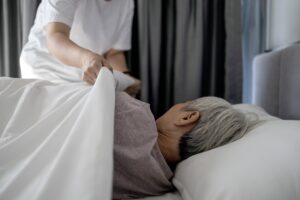 A caregiver tucking a senior woman into bed