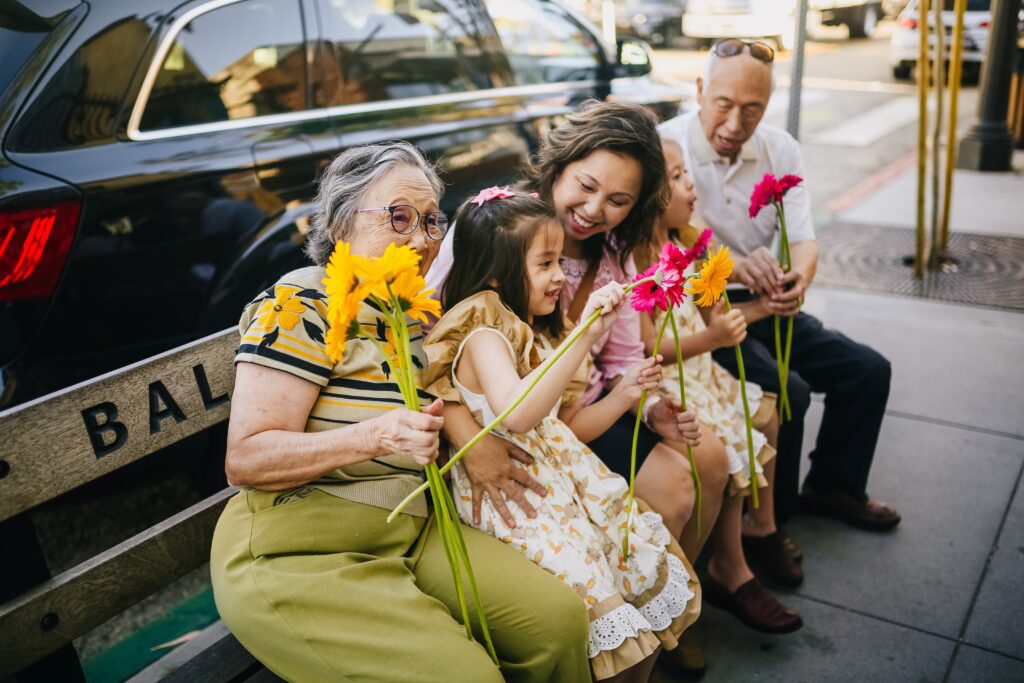 A multigenerational family sitting outdoors, highlighting the idea of living with aging parents