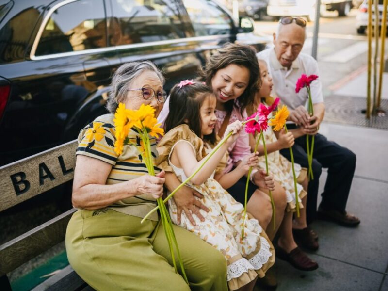 A multigenerational family sitting outdoors, highlighting the idea of living with aging parents