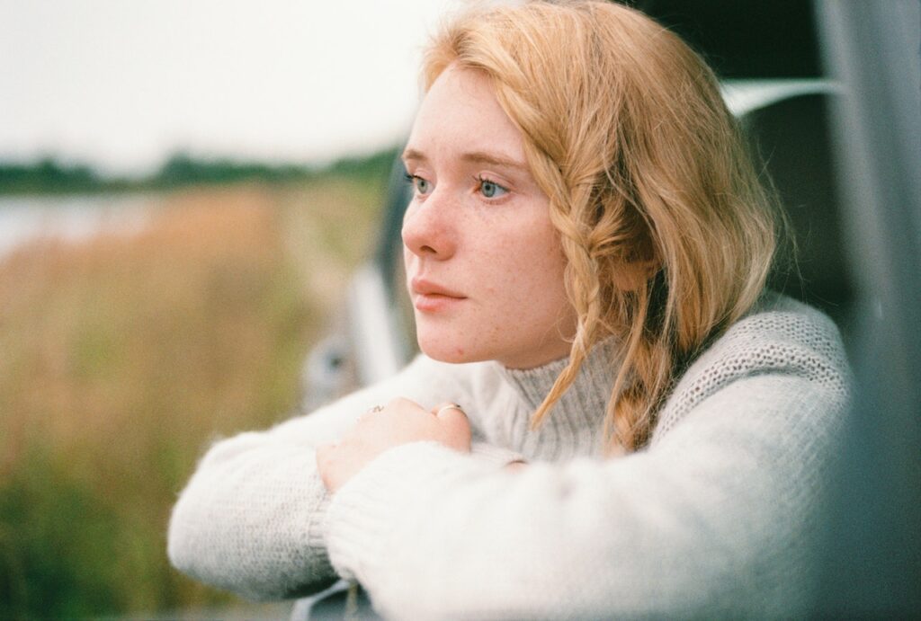 A fairly young woman thinking about what her next steps are, looking out of a car window onto fields