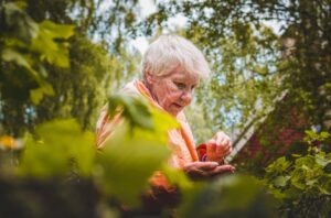 A senior woman outside seen through leaves, highlighting the idea of irrational elderly parents