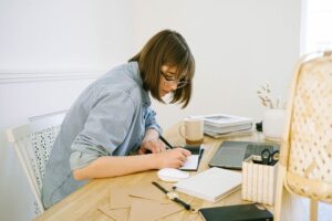 A woman writing notes on a cluttered desk, highlighting one of the challenges that millennial caregivers face