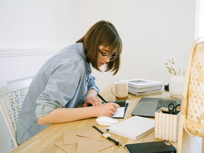 A woman writing notes on a cluttered desk, highlighting one of the challenges that millennial caregivers face