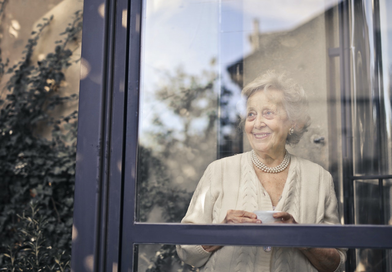 An older woman looking out the window of a senior living facility