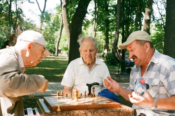 Three older men playing chess in the park, highlighting how social connections can be a type of mental health support for seniors