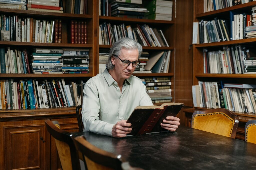 A gentleman in a library reading a book, highlighting the benefits of education for seniors