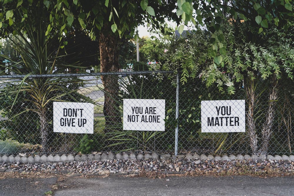 Three signs on a fence, all speaking to mental health