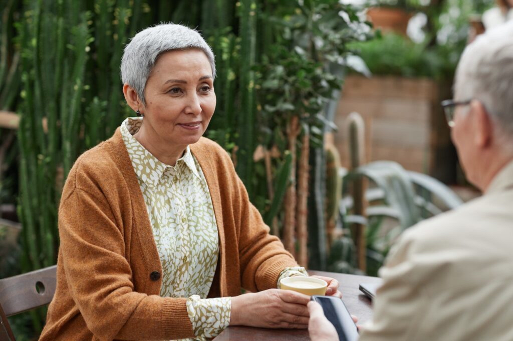 Two seniors talking across a table, highlighting the idea and the importance of end-of-life dementia conversations or other difficult conversations, like those about HIV