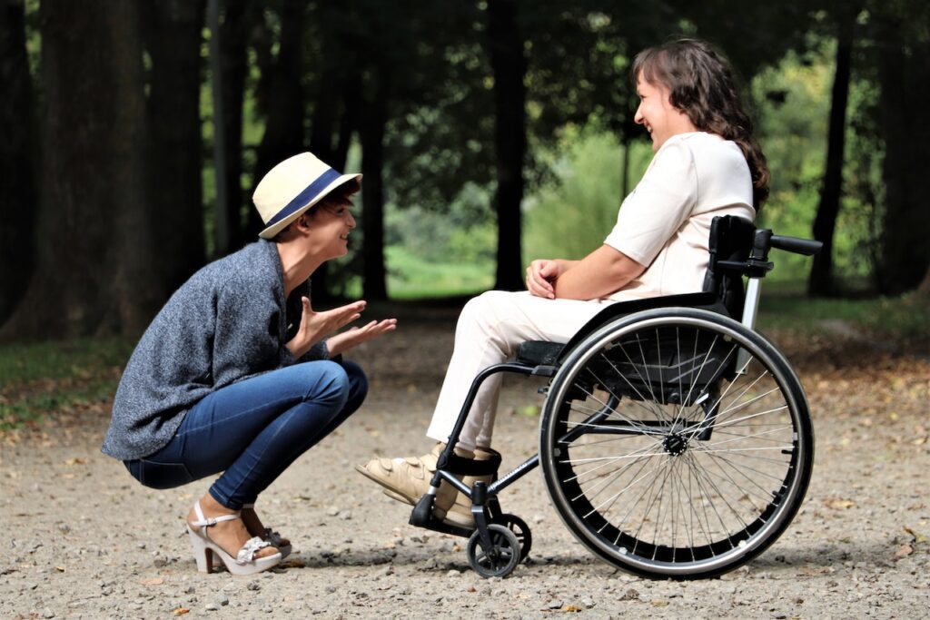 A young woman crouching in front of a wheelchair, highlighting the idea of unconventional caregivers