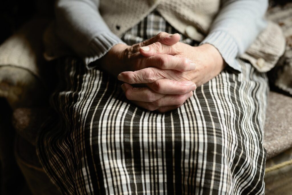 An elderly woman sitting with her hands clasped together, considering the ways that aging parents recover after serious accidents and injuries