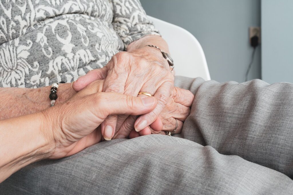 A seated woman with her hands folded, where someone is holding one of her hands, highlighting the idea of activities for seniors with limited mobility