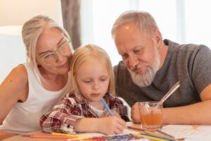 Two grandparents sitting with their granddaughter while she is drawing