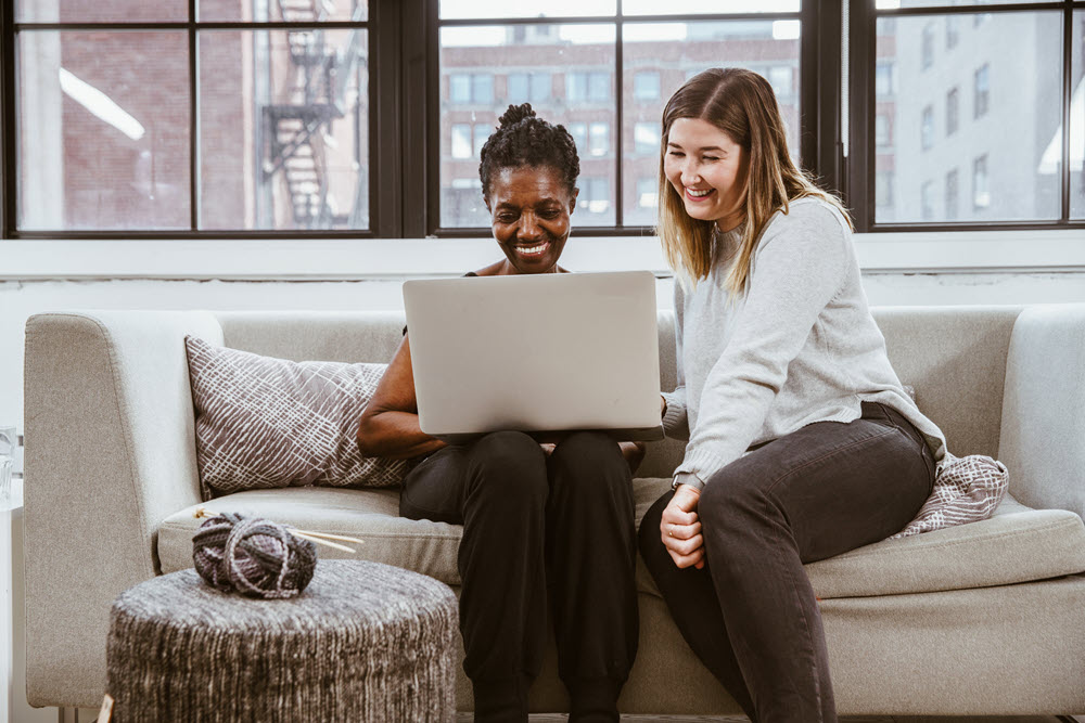 A senior and a younger friend or caregiver looking at a laptop, highlighting the benefits of technology for aging parents. 