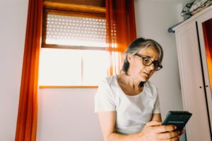 A stressed woman looking at her phone, highlighting the question of what to do if your elderly parent is being scammed