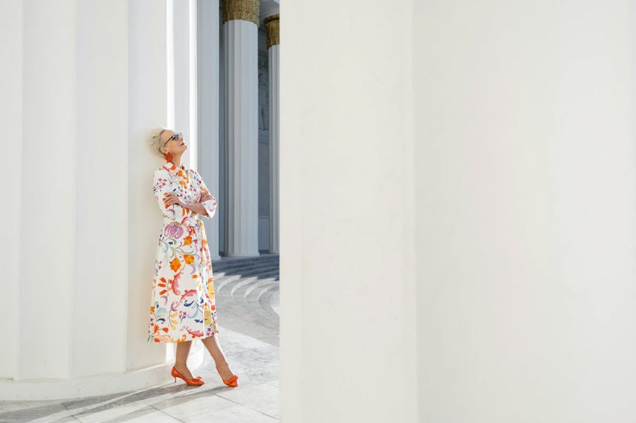 An older woman leaning against white pillars