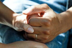 People clasping hands, where one is wearing a wedding band, highlighting the idea of cancer