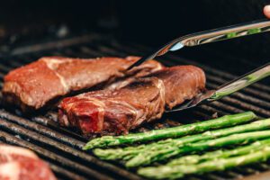 Someone grilling steak and asparagus, as an example of attractive grilling gifts for men