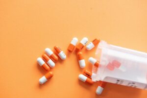 Orange and white pills spilling out of a container onto an orange background, highlighting the challenges of antipsychotics and dementia care