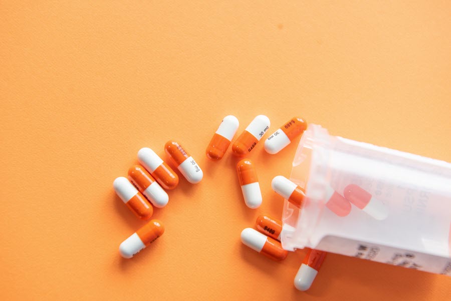 Orange and white pills spilling out of a container onto an orange background, highlighting the challenges of antipsychotics and dementia care