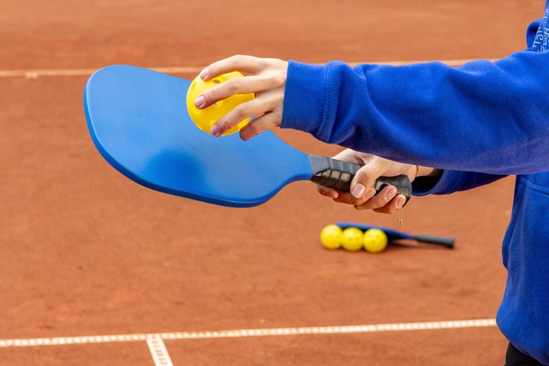 Someone holding a ball to a pickleball racquet on a court