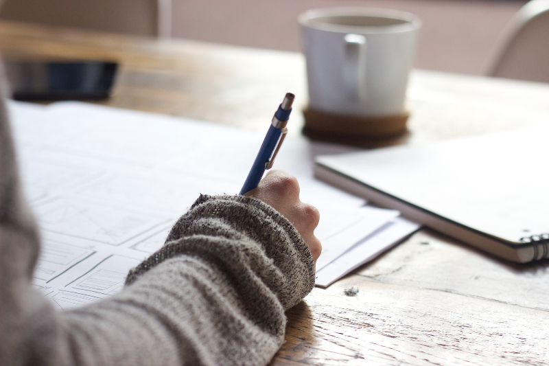 Someone wearing a jumper, looking at finances, highlighting the power of grants for seniors. There is a pad and a coffee mug on the same table, slightly out of focus. 