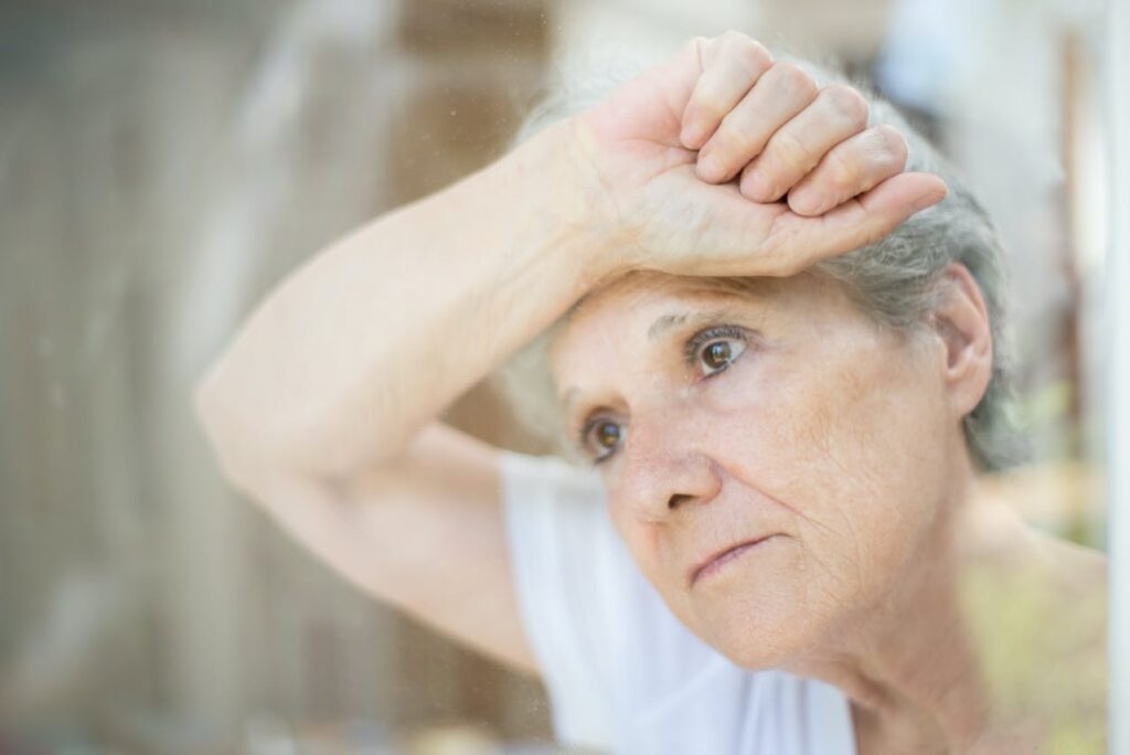 A woman leaning against the window with her wrist and forearm on the glass, highlighting the idea of senior anxiety