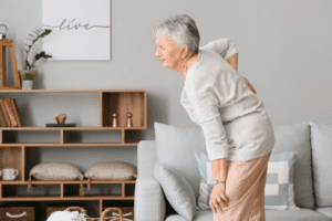 An older woman holding her back after getting up from a couch